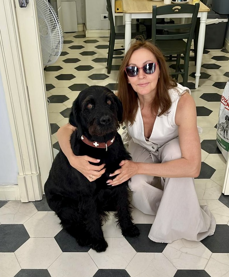 Lilia kniet neben ihrem schwarzen Hund in einem hellen Innenraum